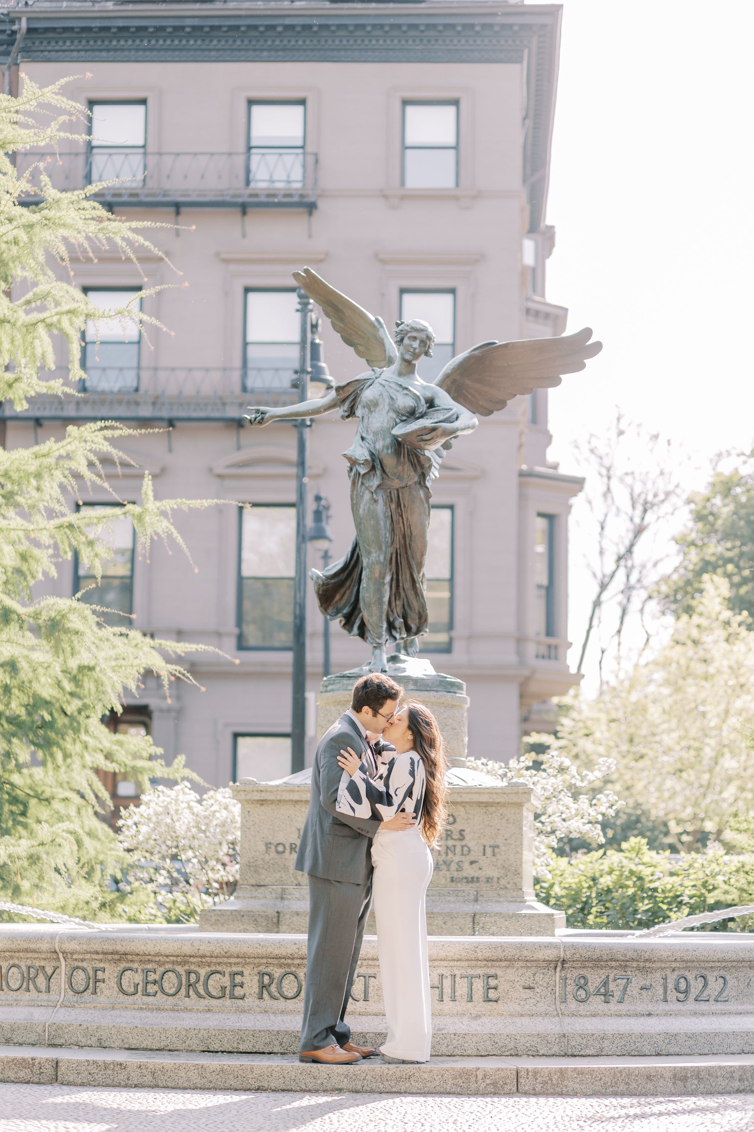 Romantic couple sharing a moment near a historic building with ornate architectural details and statues.