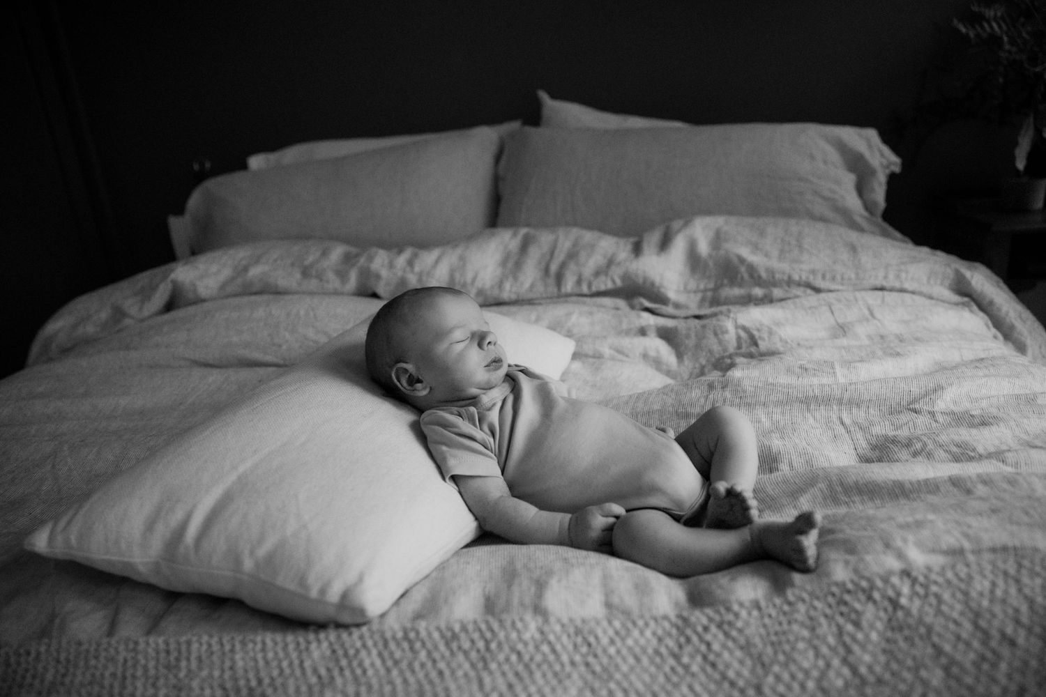 Baby lying on white bedding in black and white portrait photo.