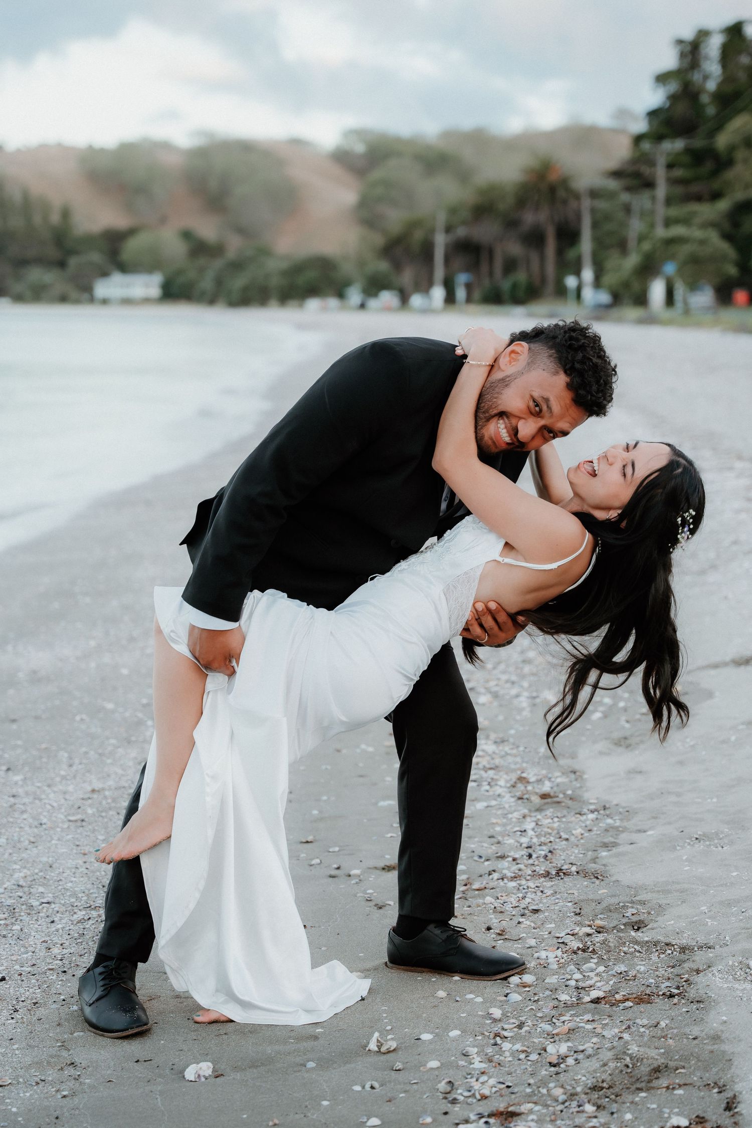 Romantic dip pose on a beach with mountains and palm trees in the background.