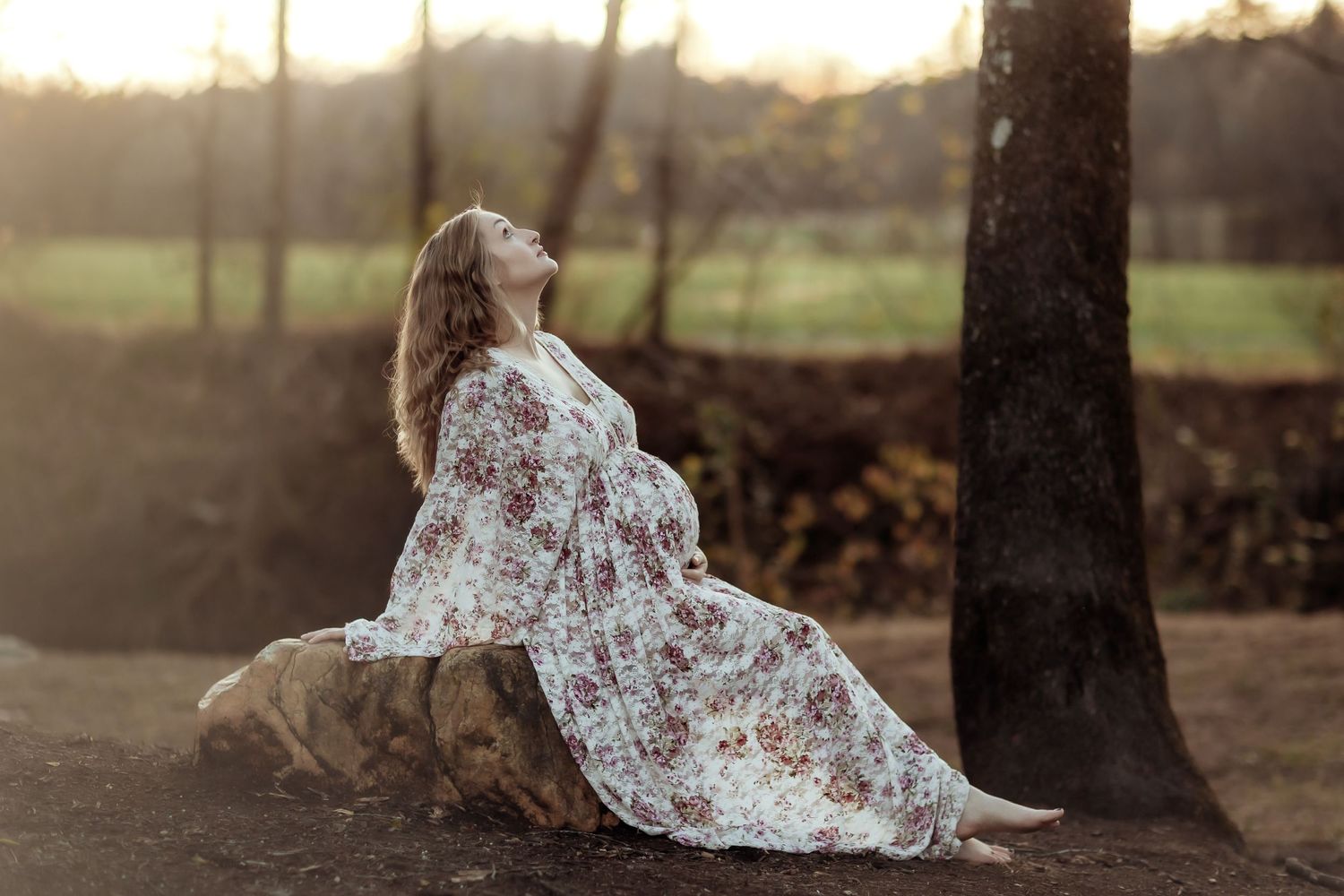 Flowing white floral dress drapes elegantly over rustic log in sunset woodland setting.