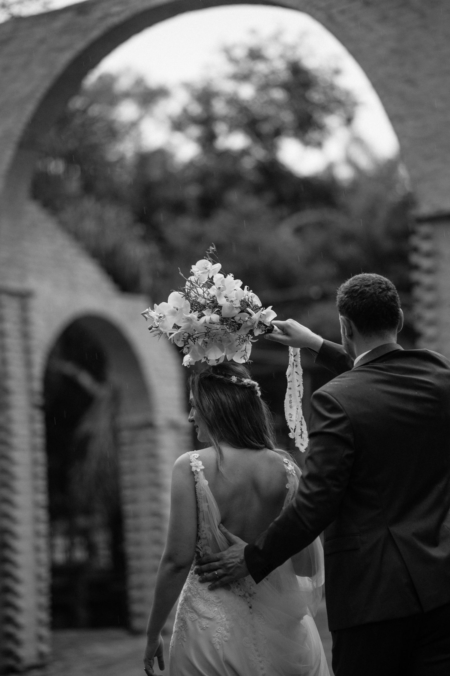 A wedding ceremony under a floral arch adorned with orange flowers and pampas grass in a garden setting.