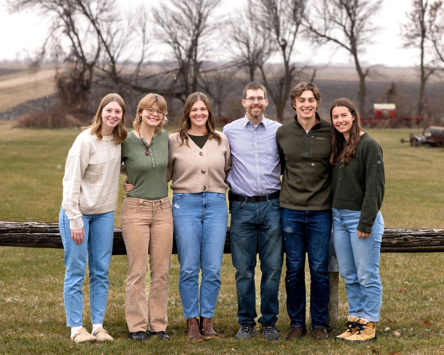 Family of six posing together in a rural farm setting with rolling hills in the background.