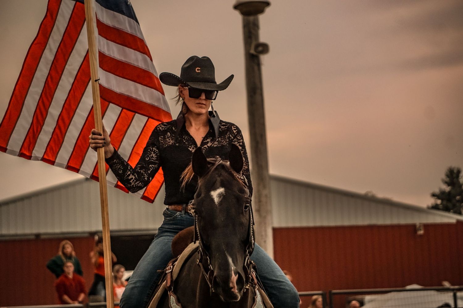 Rider on horseback carrying an American flag at a western rodeo event.