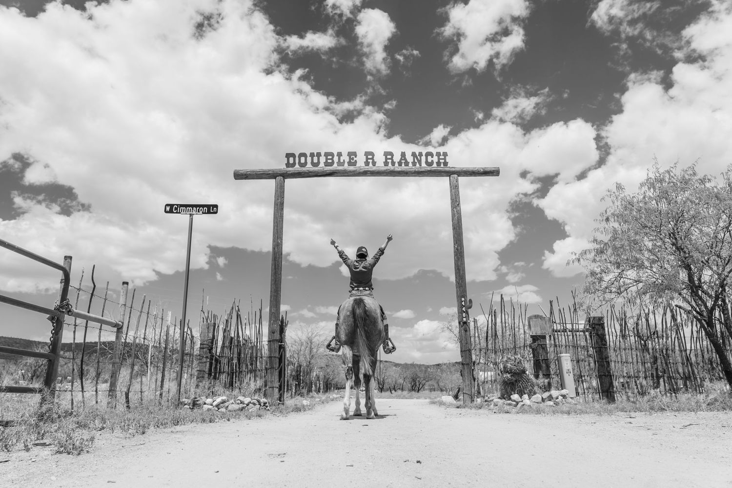 Black and white photo of a rider celebrating under the Double R Ranch entrance gate.