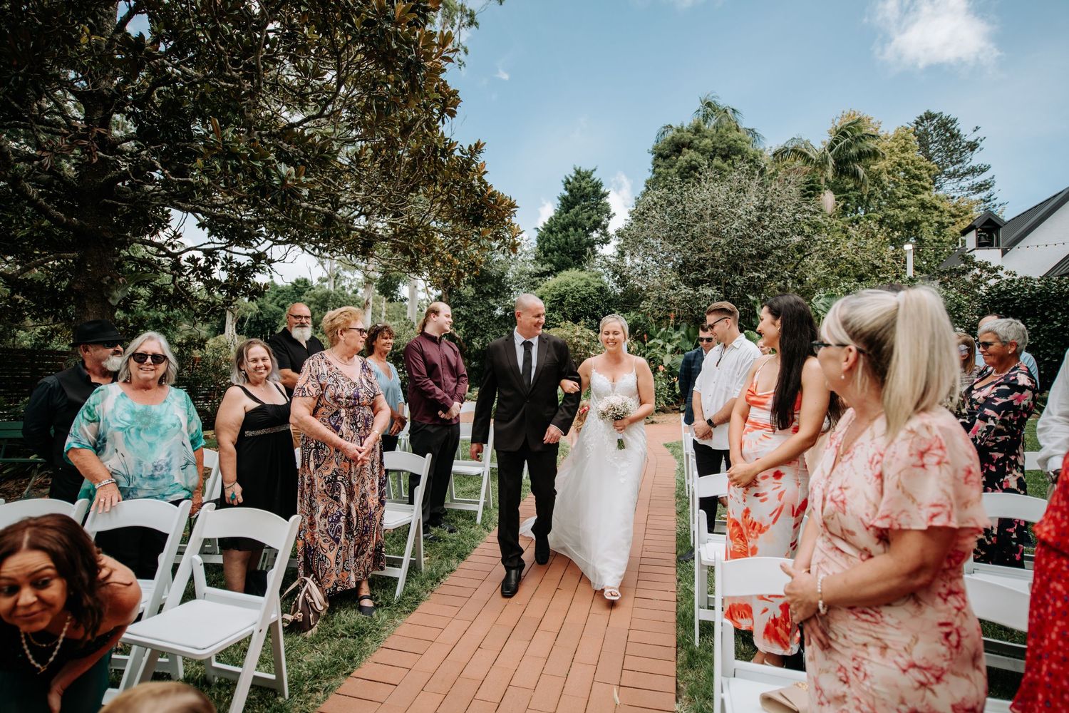 Guests seated in white chairs during an outdoor wedding ceremony on a wooden deck.