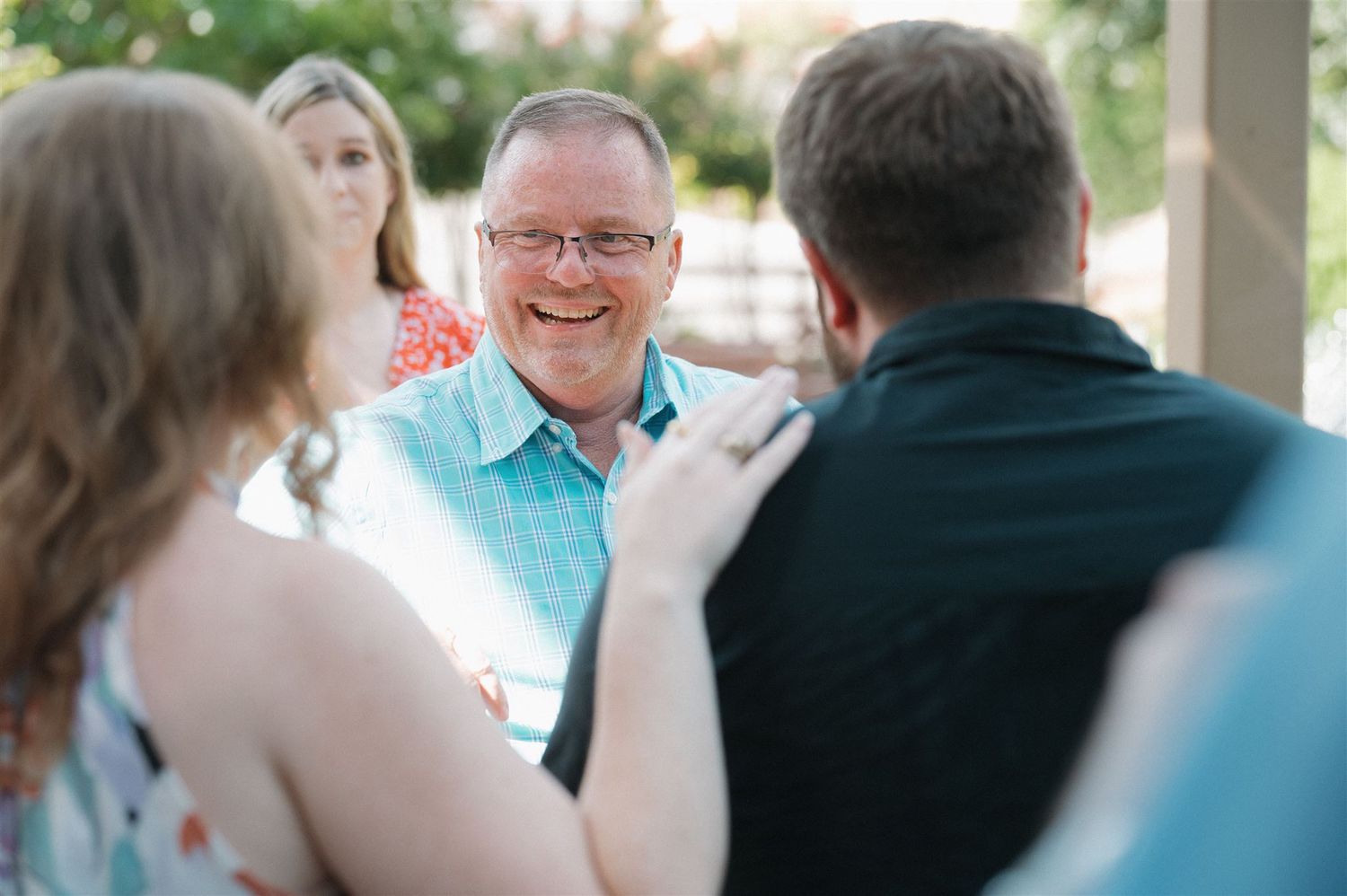 A cheerful conversation between a small group of people on a covered porch during a sunny day.