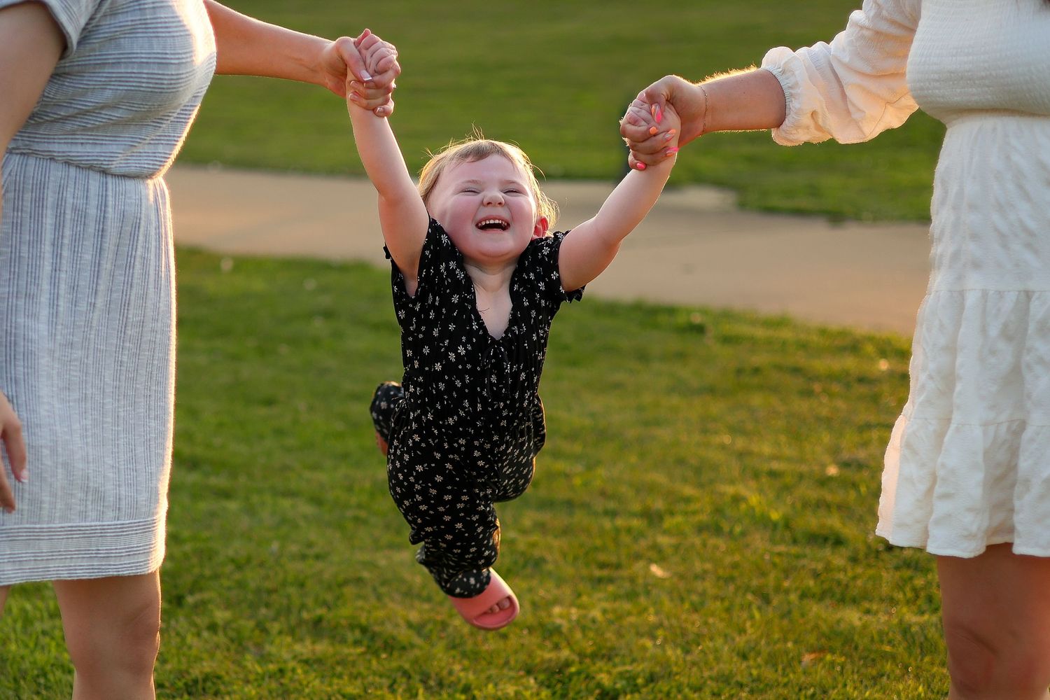 Joyful moment captured as small child swings between two people outdoors.