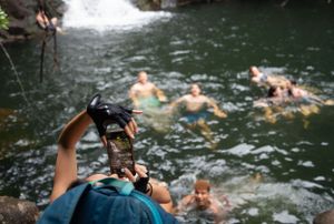 Swimmers playing and splashing in a natural pool beneath a waterfall.