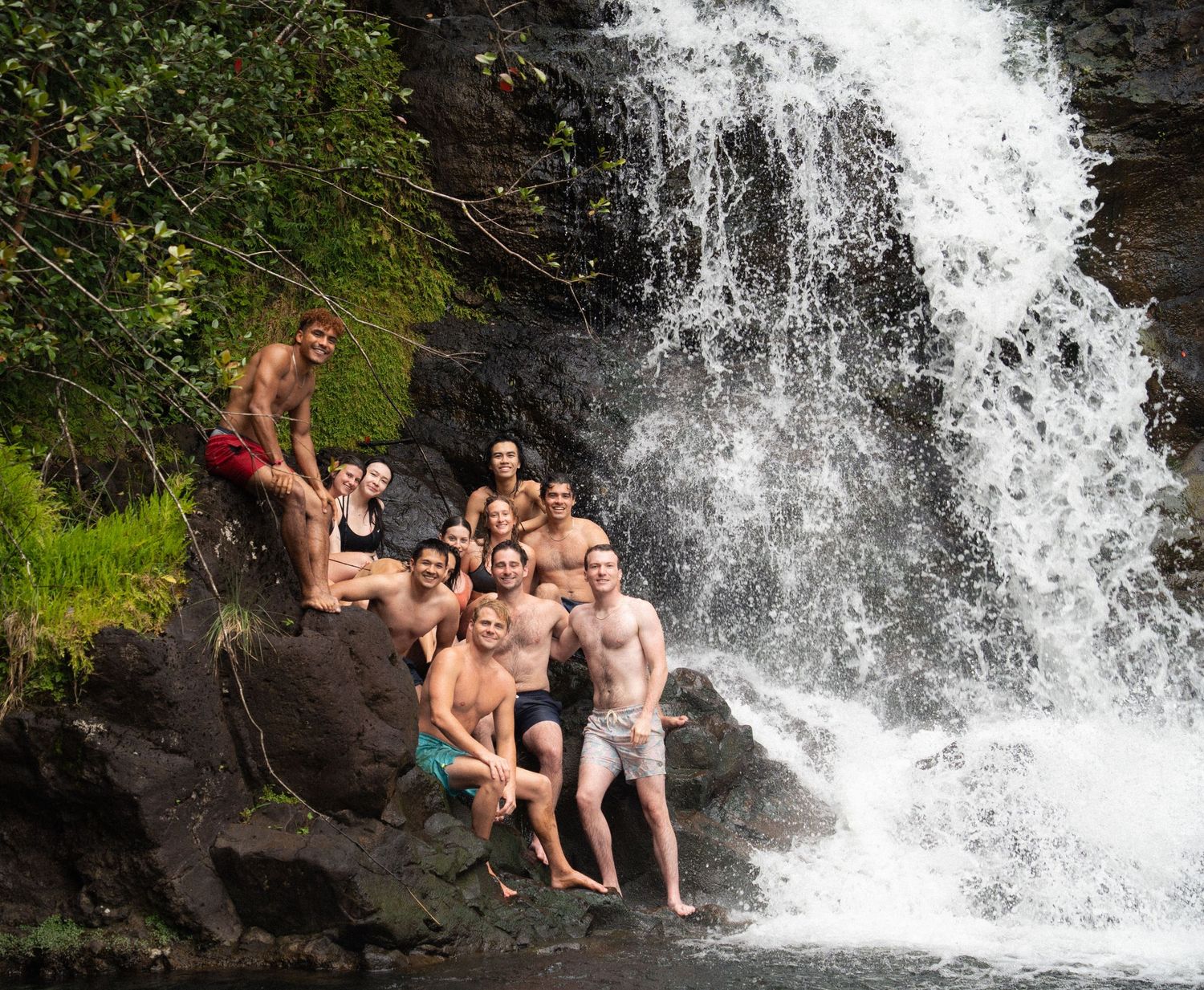 People enjoying a refreshing swim and splash at a scenic waterfall surrounded by lush greenery.