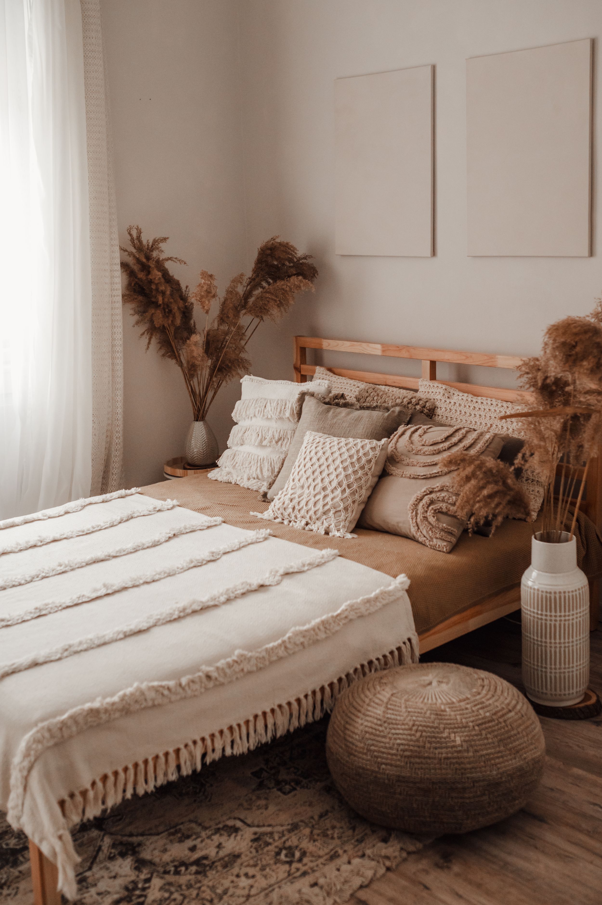 Boho bedroom with wooden bed frame, textured linens, and pampas grass decor.