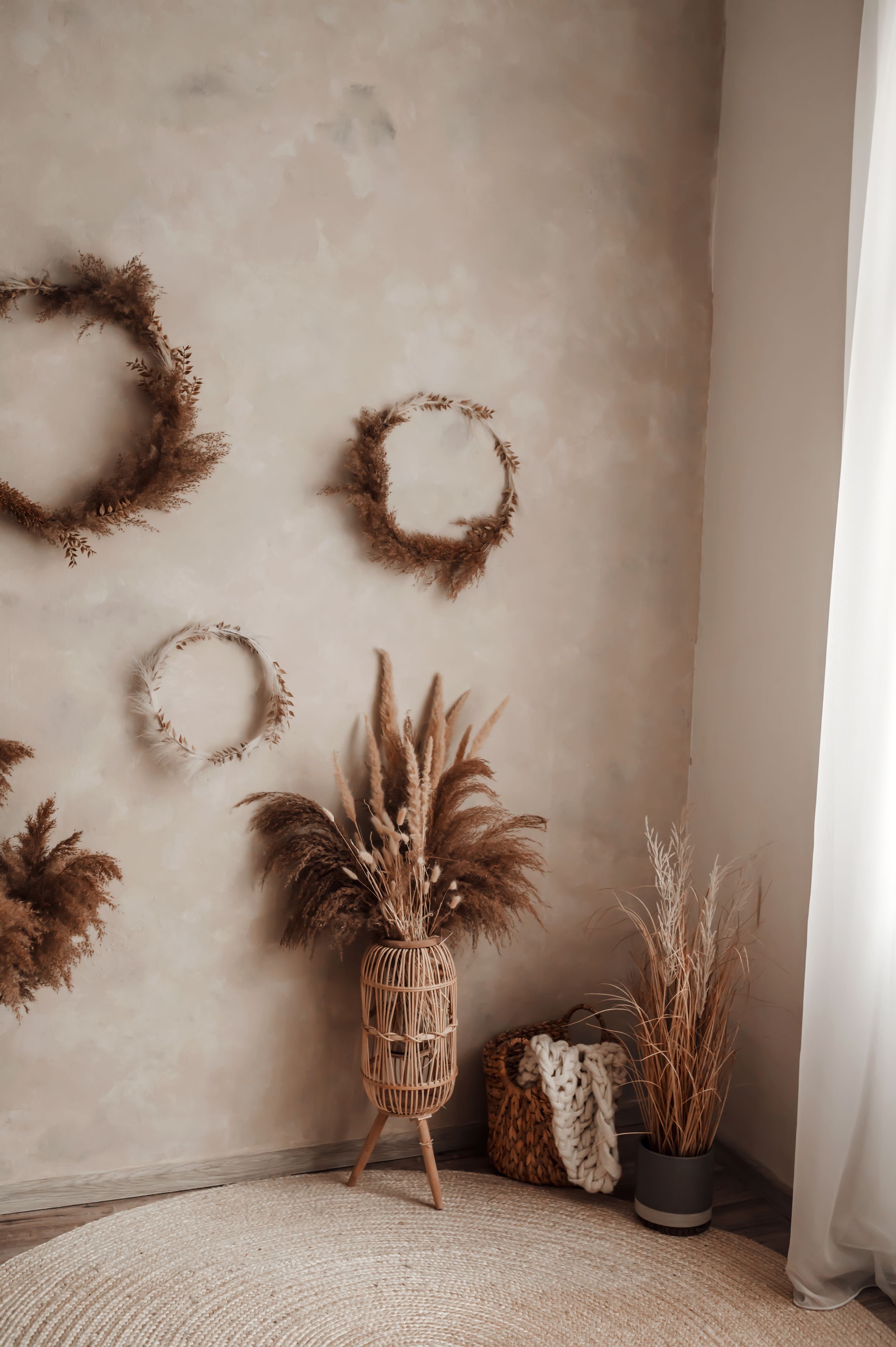 Boho living space with dried floral wreaths on wall and woven vase with pampas grass.
