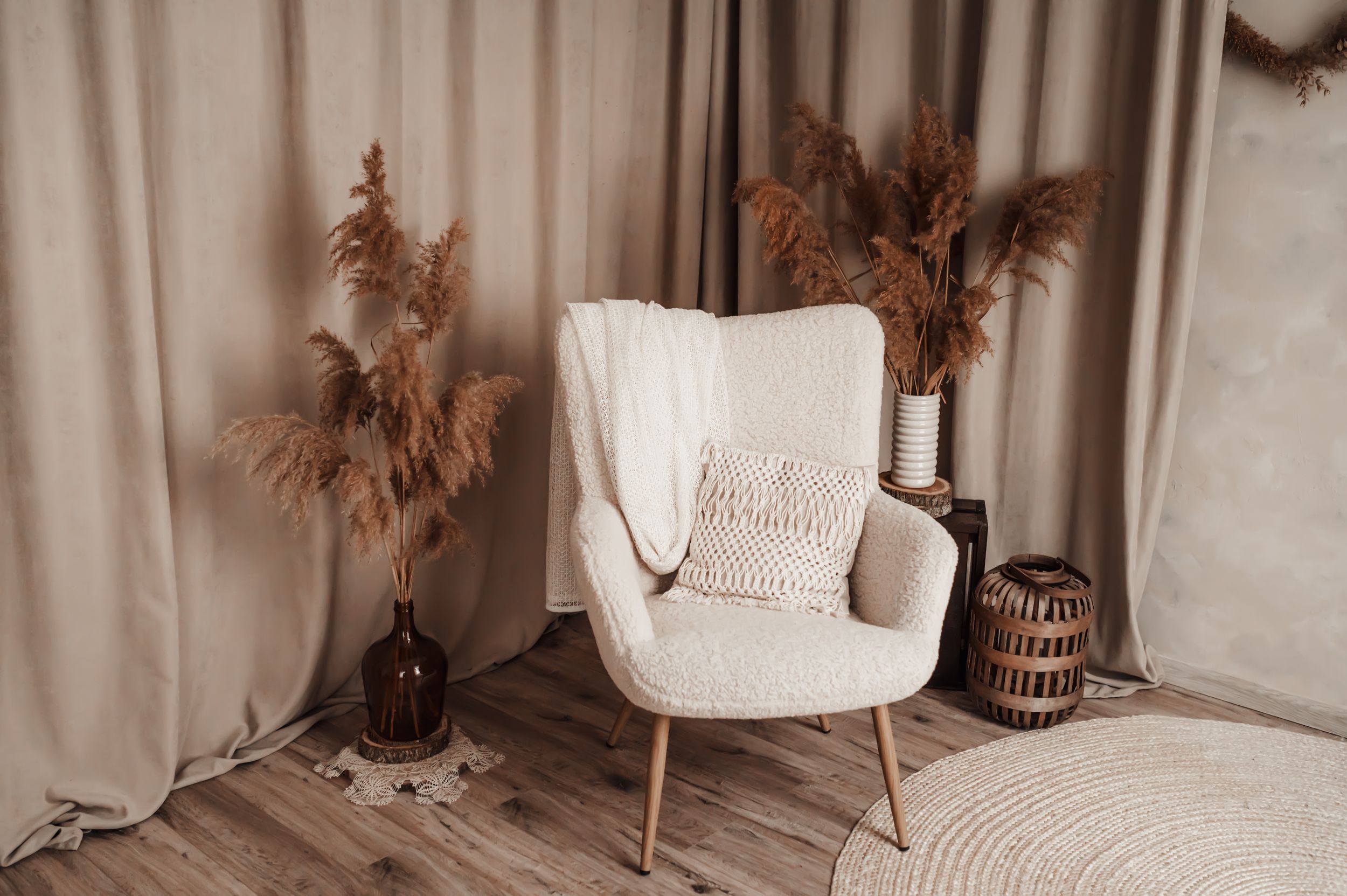 White armchair with decorative pampas grass and woven baskets in a neutral-toned corner.