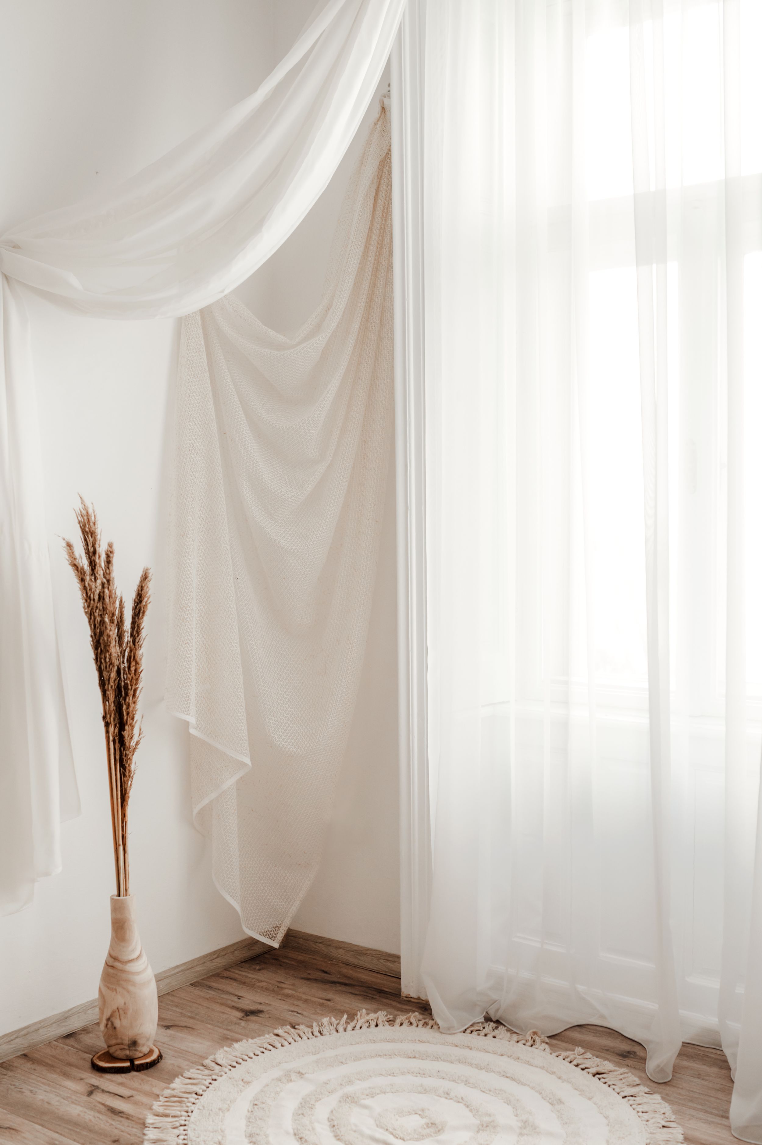 Minimalist interior with white flowing curtains and dried pampas grass in vase.