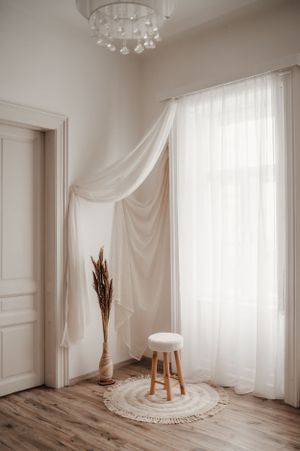 Minimalist room corner with sheer white curtains, round rug, and crystal chandelier.