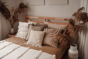 Bedroom with wooden headboard, textured pillows, and dried pampas grass arrangements.