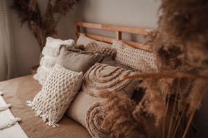 Close-up of bed with knitted pillows and natural brown tones against white wall.