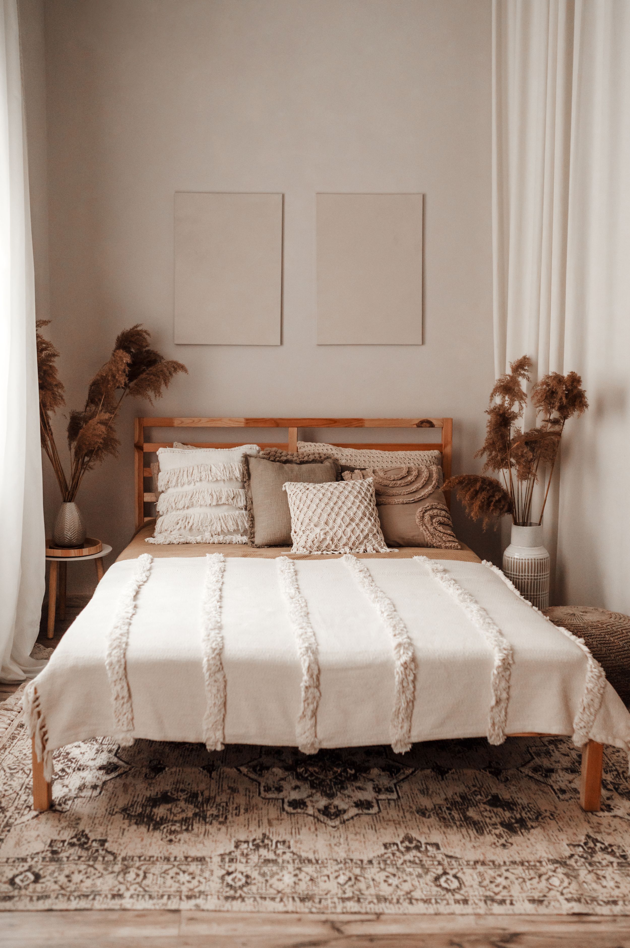 Cozy neutral bedroom with wooden bed frame, textured bedding, pampas grass decor and vintage area rug.