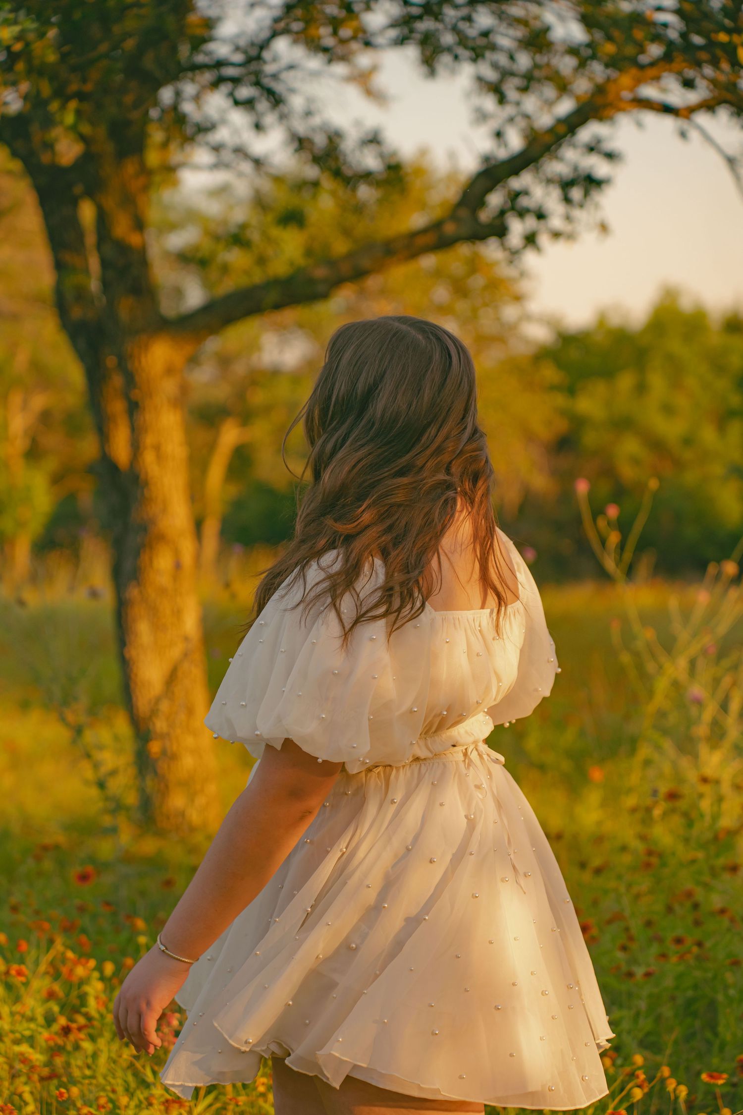 A person in a flowy white dress twirls in a sun-dappled autumn garden setting.
