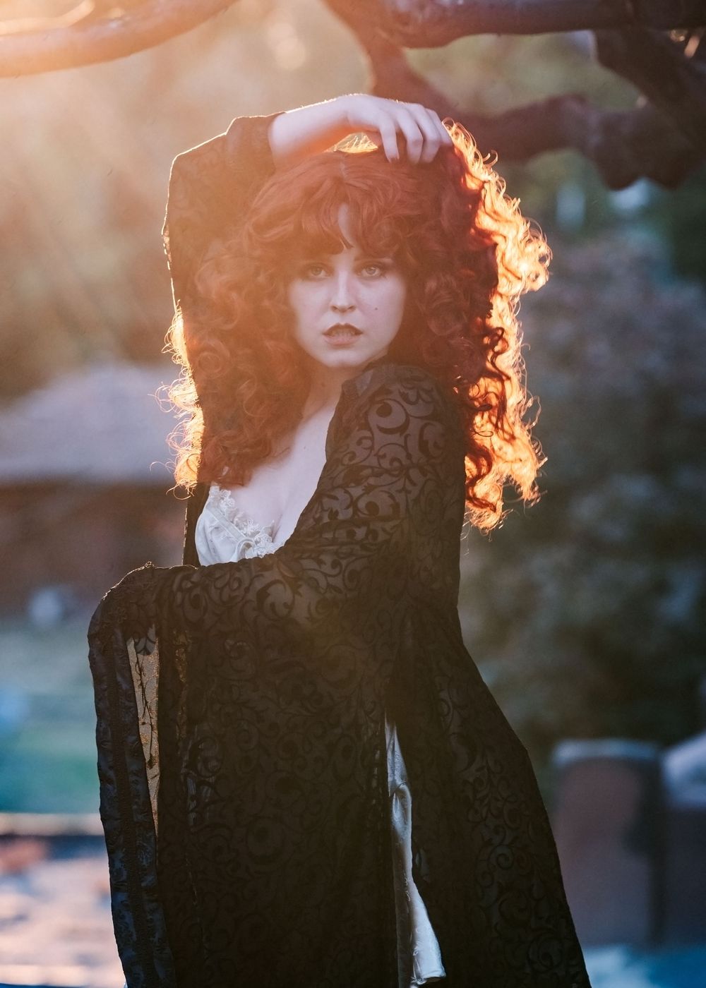 Backlit portrait of a woman with curly hair wearing a black lace dress in golden sunlight.