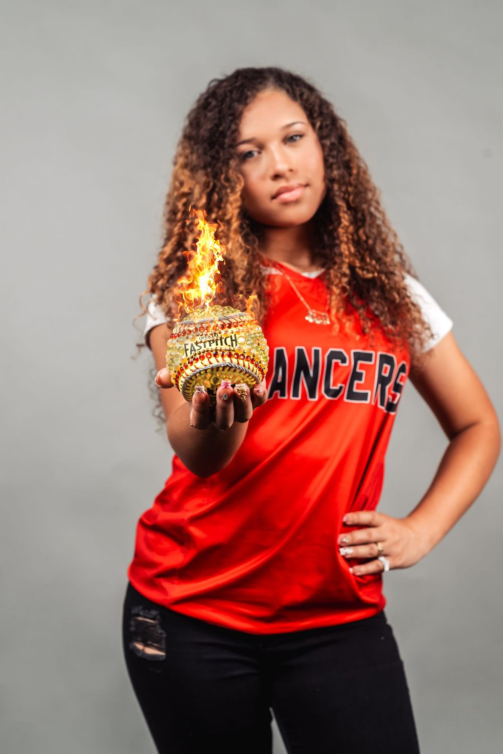 Athlete in red jersey holding a flaming softball trophy against gray background.