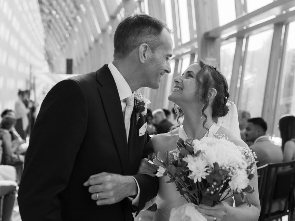 Black and white wedding photo of smiling bride holding bouquet and groom in suit sharing a tender moment.