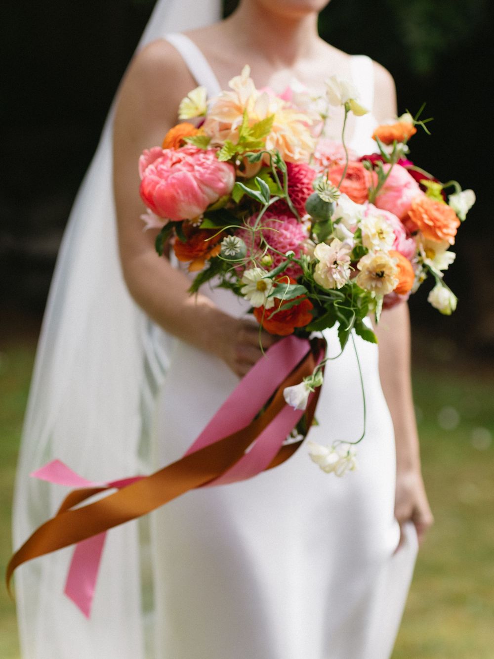 Bride in white gown holding a vibrant pink and orange wedding bouquet with flowing silk ribbons.
