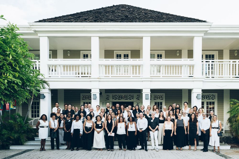 Large group in black and white formal attire posing in front of elegant white colonial-style building.