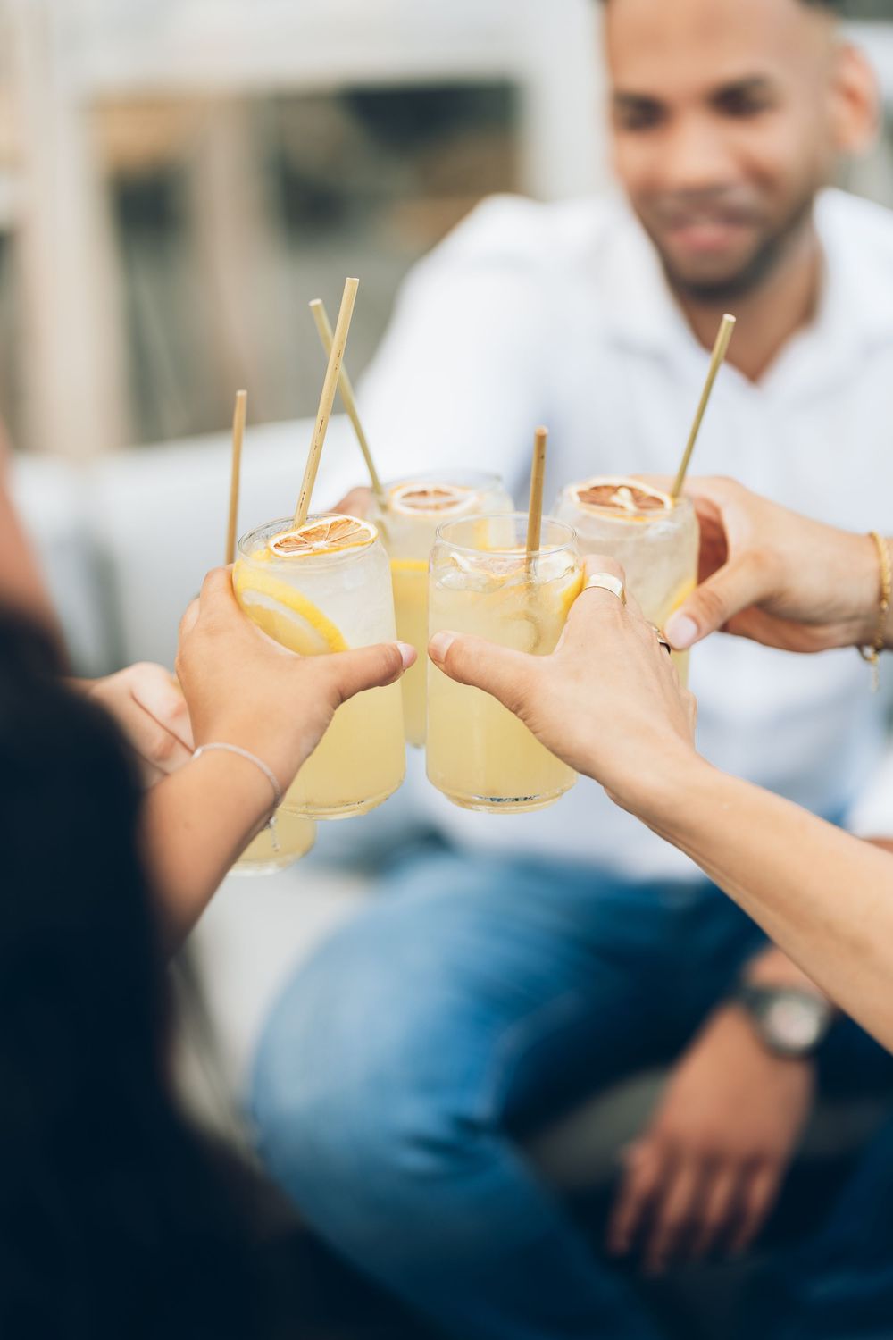 Friends clinking glasses of fresh lemonade with straws and citrus slices at an outdoor social gathering.