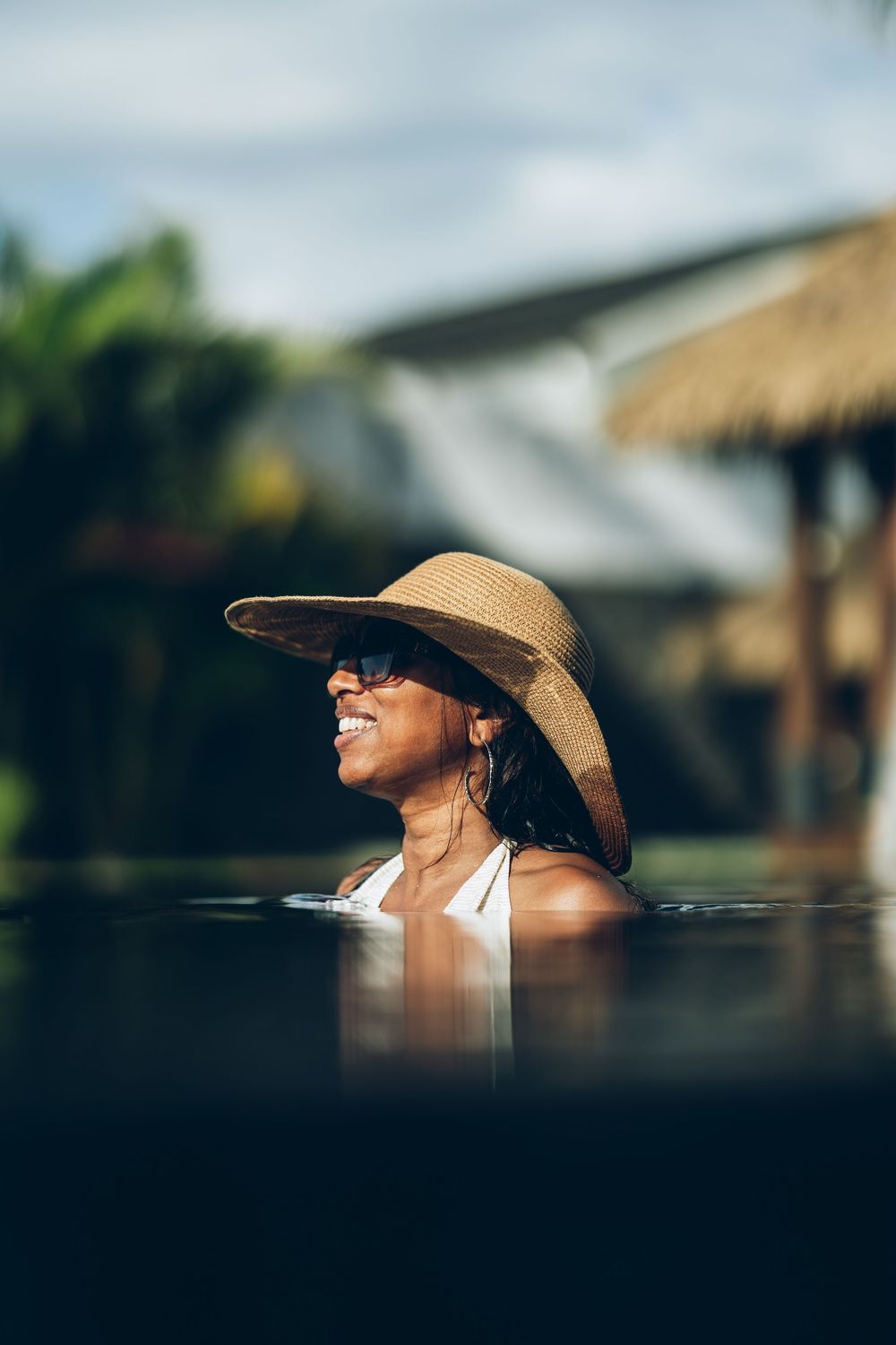 A person wearing a wide-brimmed sun hat smiles while enjoying a sunny day outdoors.