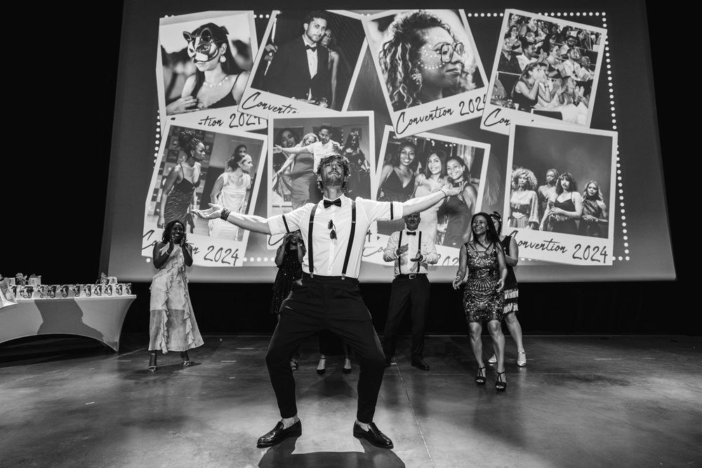 A black and white photo shows performers on stage with vintage photographs projected behind them during a theatrical show.