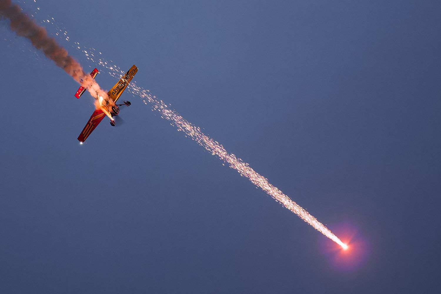 An aircraft releases bright red flares during a nighttime aerial display.