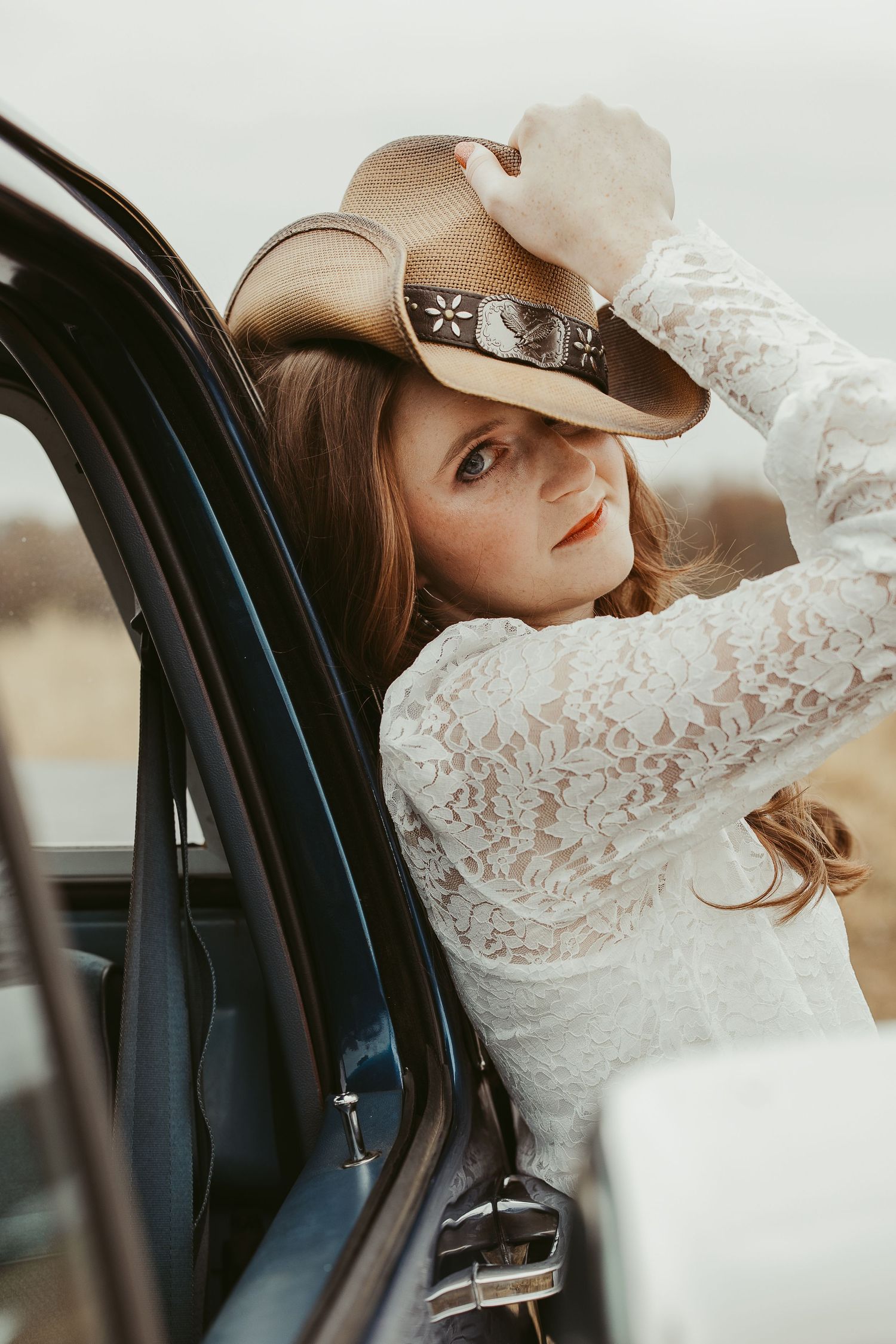 Close up view of someone wearing a brown hat and white lace dress in a car.