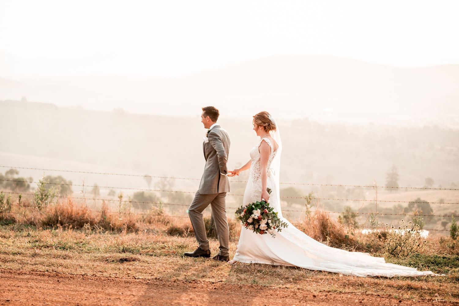 Couple in wedding attire standing on hilltop at sunset with scenic mountain landscape in the background. Brisbane, Gold Coast Sunshine Coast