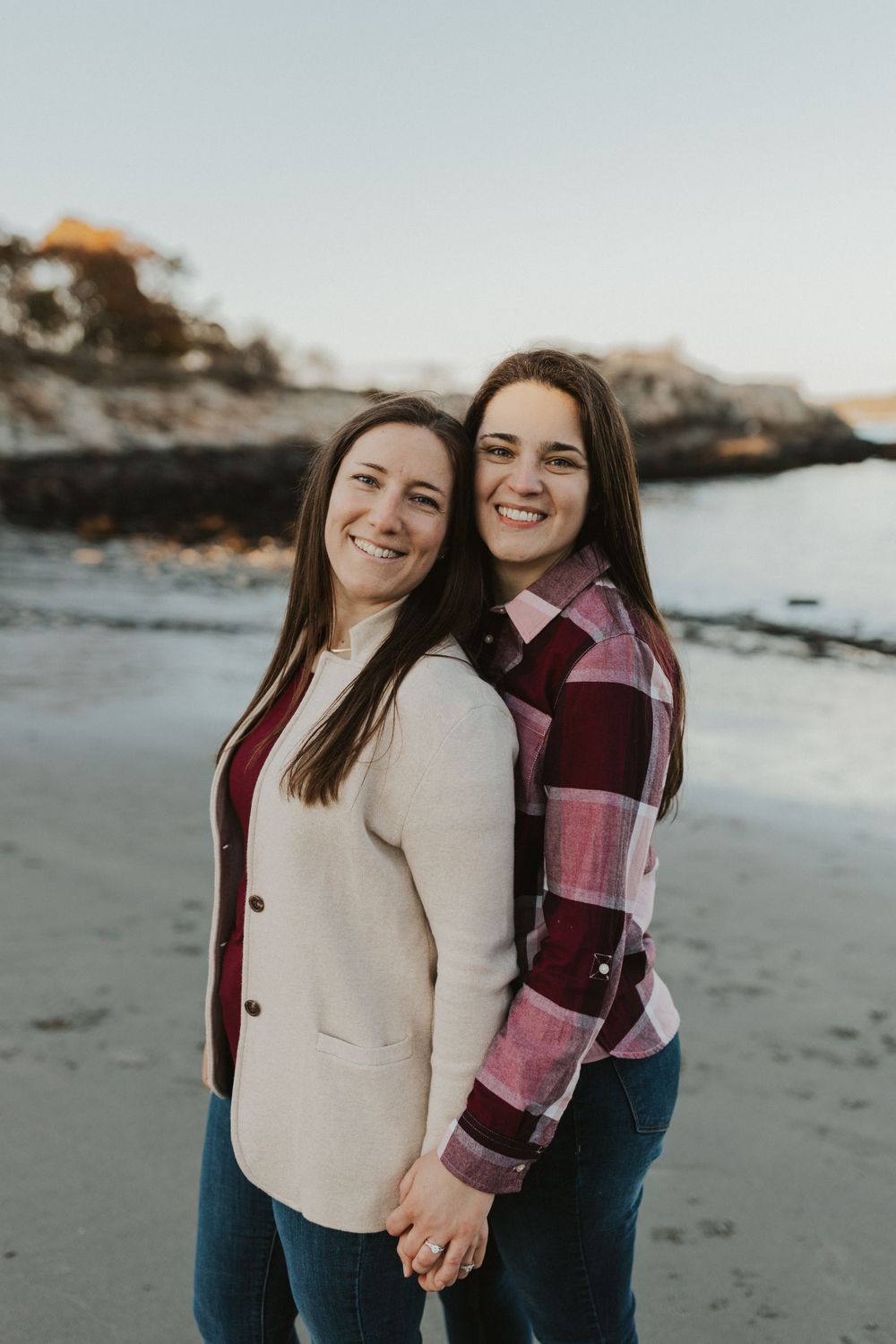 A couple posing together on a beach at sunset with coastal rocks in the background.