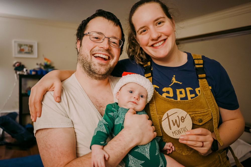 Happy family with two-month-old baby holding milestone disc.