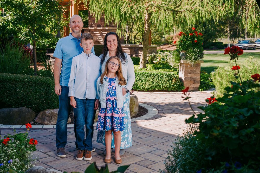 Family of four standing together in a vibrant garden with red flowers nearby.