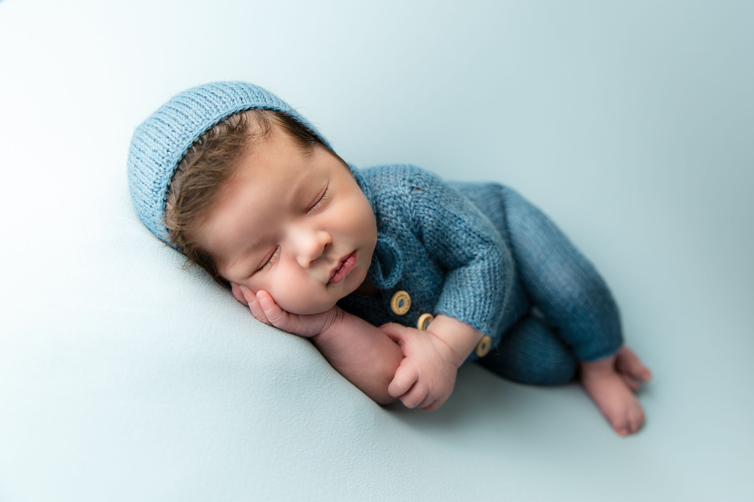 Sleeping newborn wearing soft blue knit outfit in minimalist photography setup.