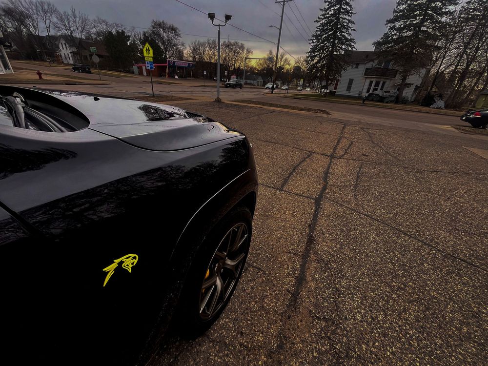 A black car with yellow accents parked in an empty parking lot at dusk.