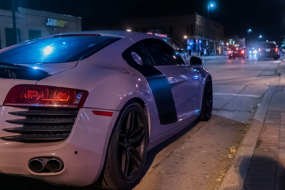 A white Audi R8 sports car parked on a city street at night with illuminated LED lights.