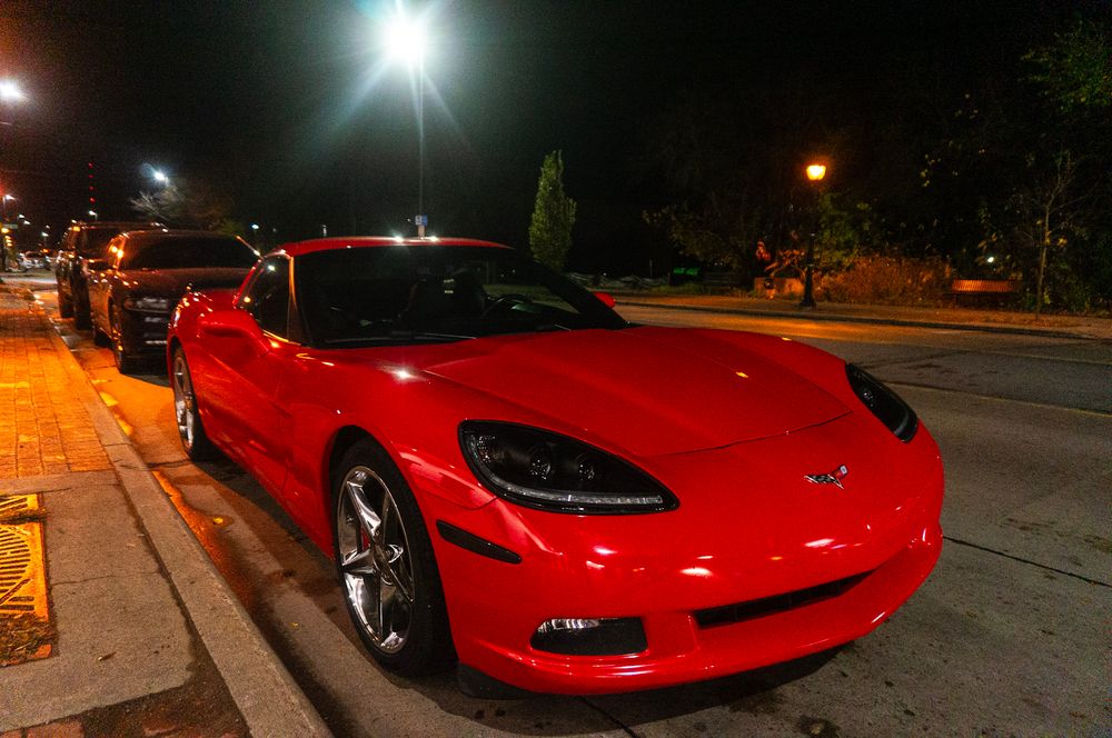 Red sports car parked at night with bright street lights illuminating the scene.