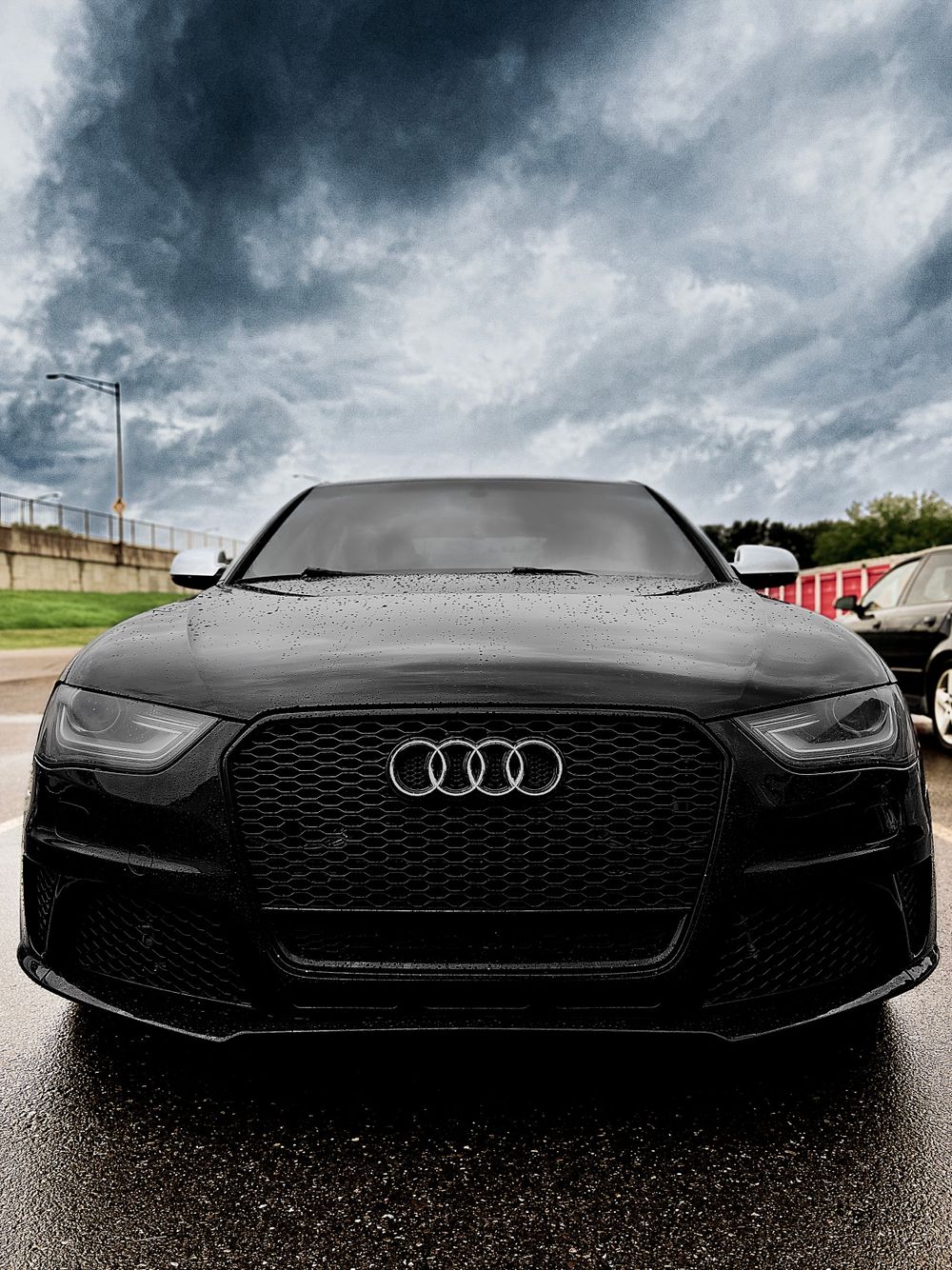 Front view of a black Audi RS with aggressive grille under dramatic stormy skies.