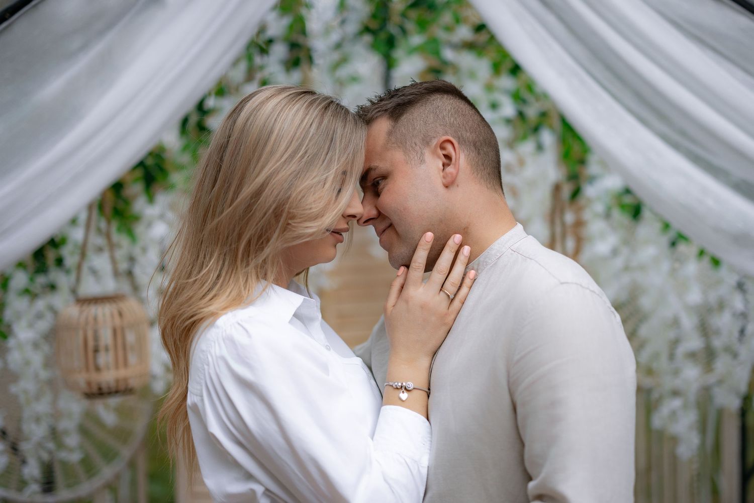 Romantic couple sharing intimate moment under white draped arch with greenery.