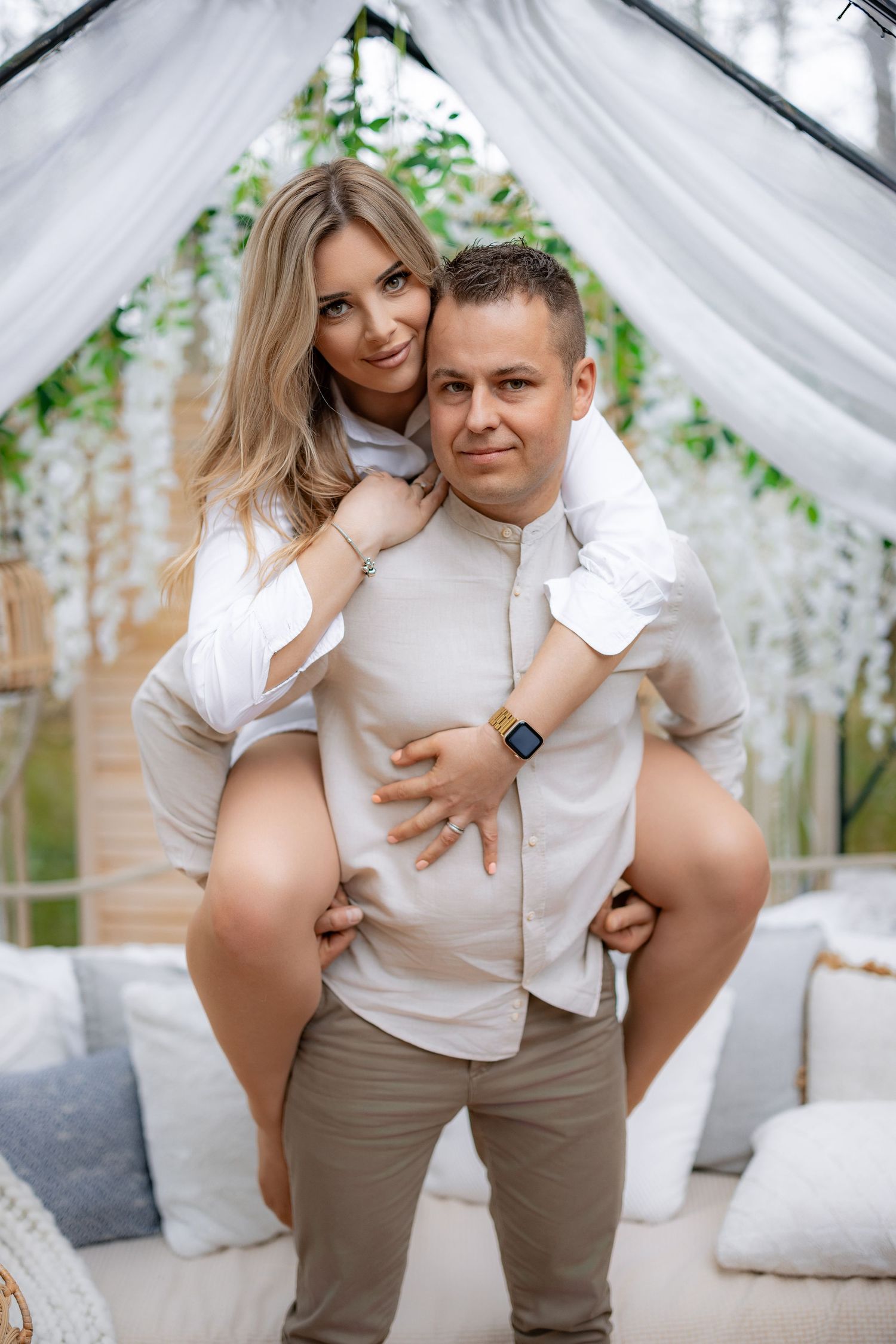 Playful piggyback pose in white-draped garden setting with hanging lanterns.