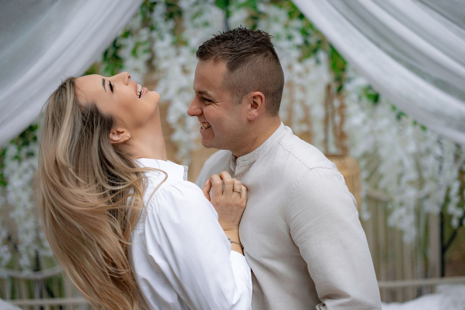 Couple laughing and embracing under white draped wedding arch.