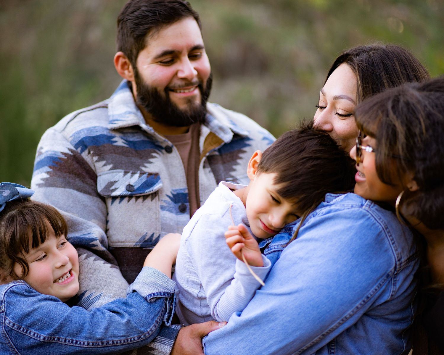 A happy family laughs and embraces together during an outdoor photo session in casual denim and sweaters.