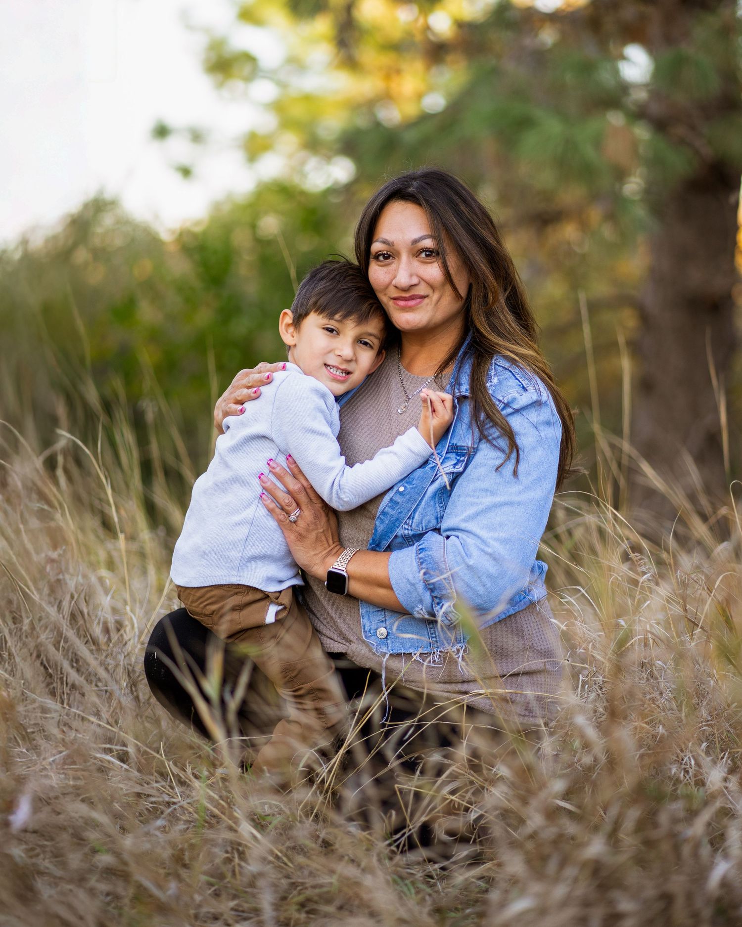 A mother and child share a tender moment while posing together in tall grass during a golden hour photoshoot.
