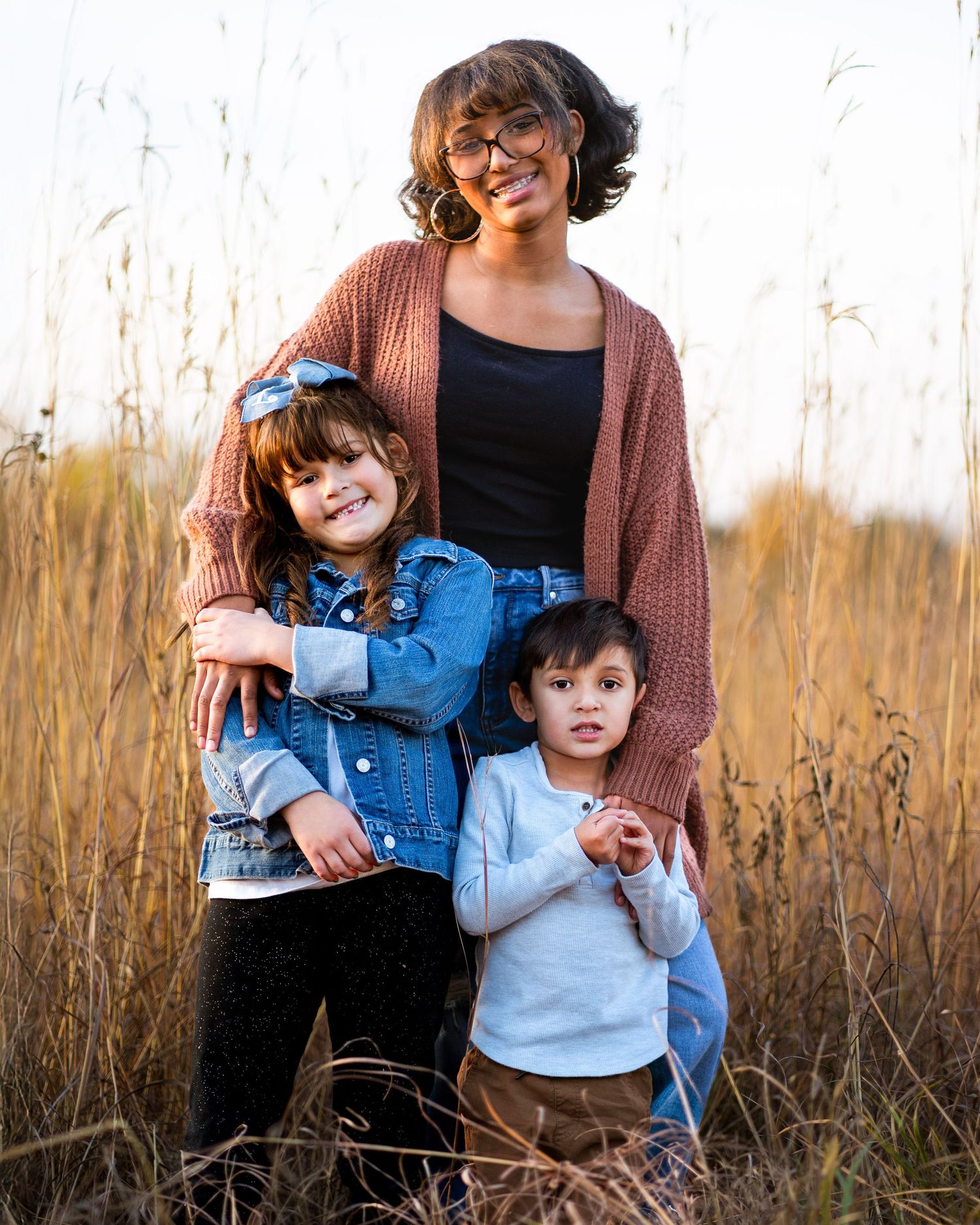 Group portrait in a golden field of tall grass during sunset wearing denim and casual attire.