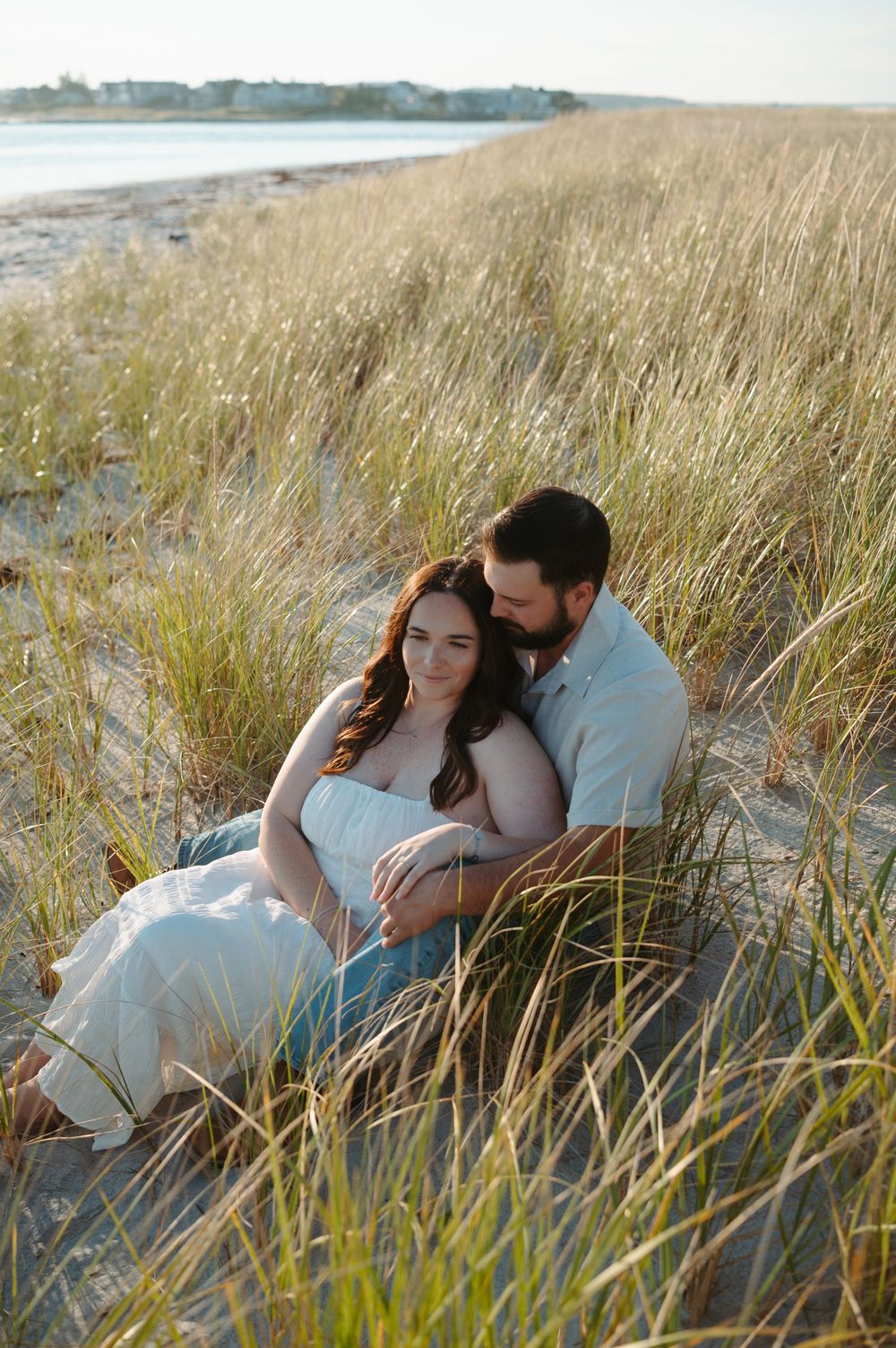 A couple shares an intimate moment together while laying in tall beach grass at sunset.