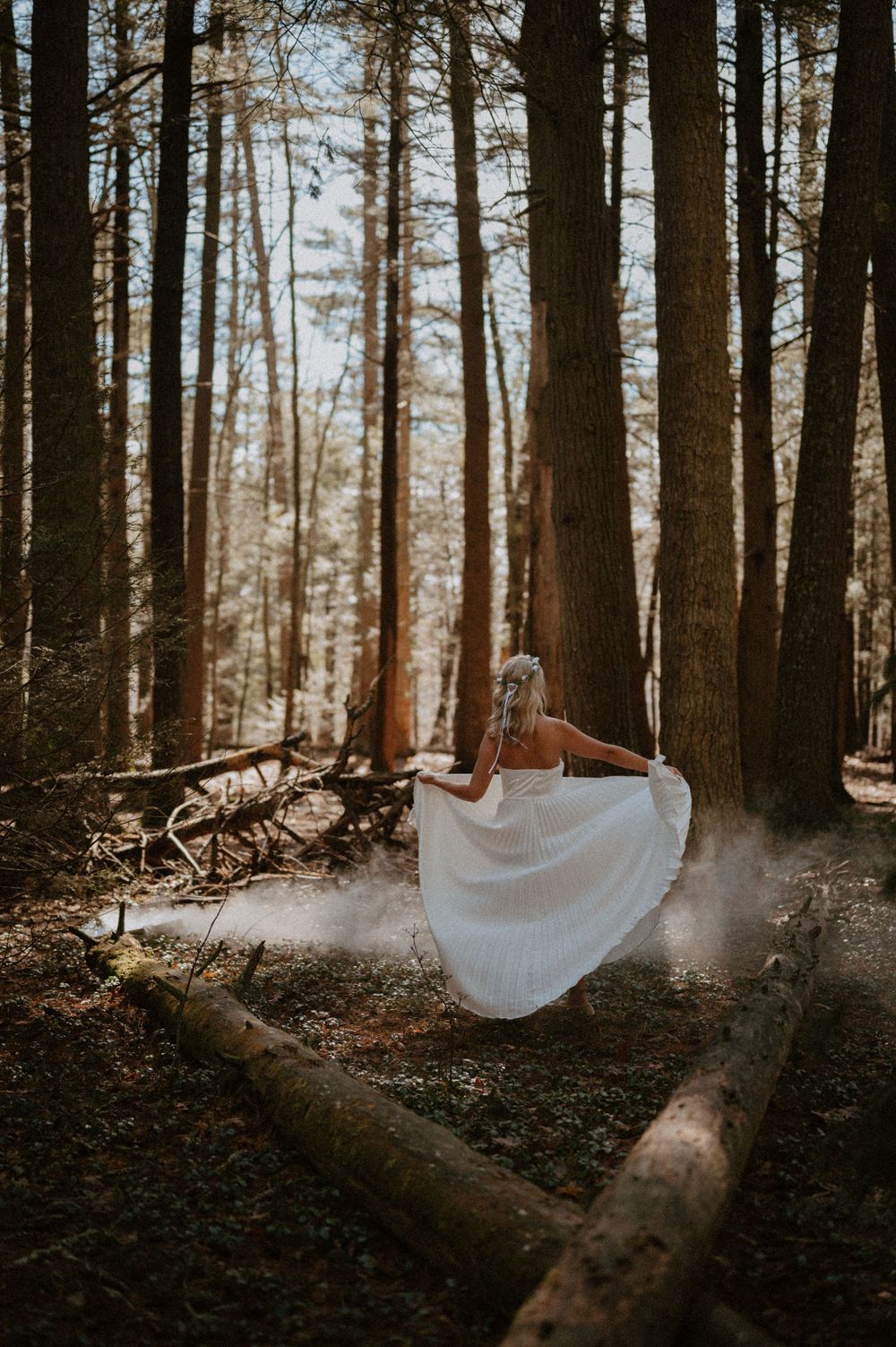 A flowing white dress floats magically above a fallen log in a mystical forest setting.