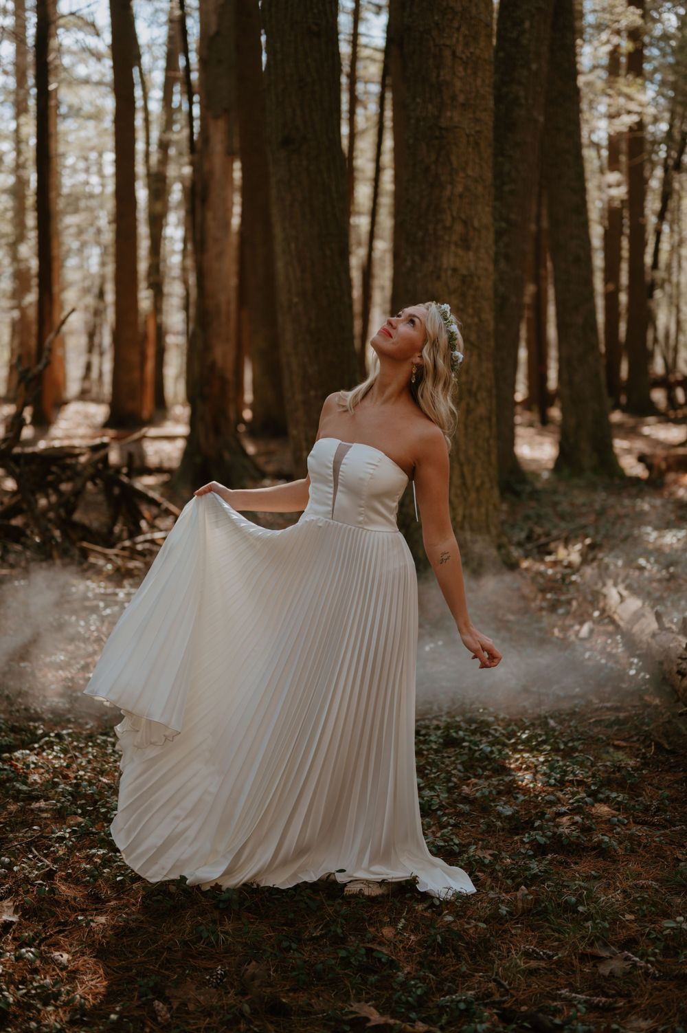 A flowing white pleated wedding dress twirls gracefully in a misty forest setting during a photoshoot.